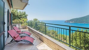 A balcony with two red lounge chairs, a tiled floor, and a view of the sea and a green hill. - Lambrusca by Interhome (Moneglia)