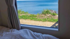 Una habitación con cama y ventana con vistas a una playa de aguas azules cristalinas y vegetación.