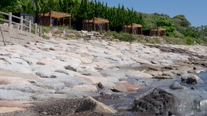 Una playa rocosa con estructuras de madera y un promontorio cubierto de bosque.