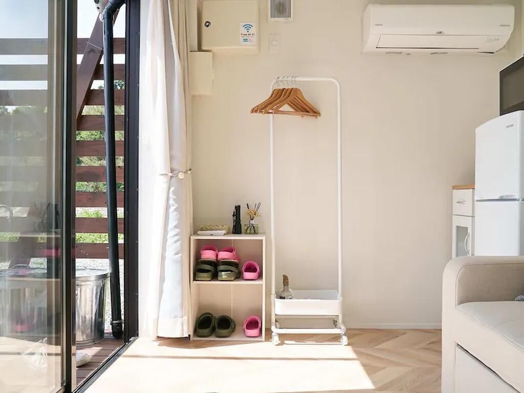 Une pièce de taille modeste avec une porte vitrée donnant sur un espace extérieur, une étagère blanche où sont rangées des chaussures, un porte-manteau en bois et une armoire blanche.
