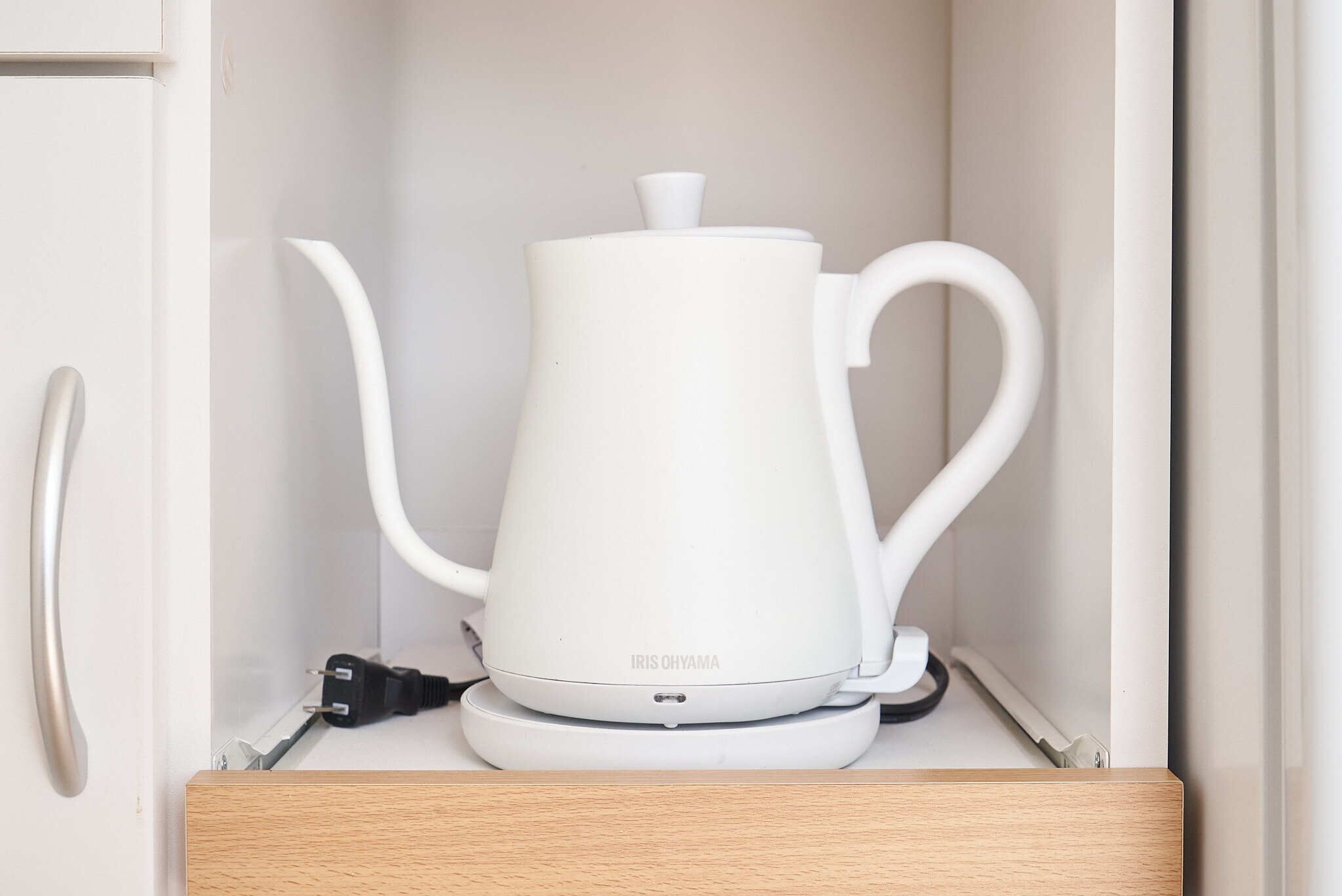 A white electric kettle with a lid and handle, placed on a white countertop.