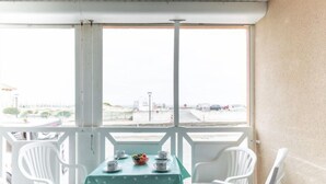 A balcony with a table set for two, white plastic chairs, and a view of the beach and parking area. - Belvédère by Interhome (Mimizan)