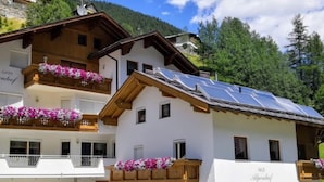 A two-story building with balconies adorned with flowers, a wooden facade, and a solar panel roof.