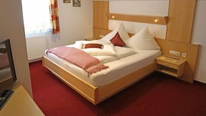 A single-bed room with a wooden headboard, a bedside table with a lamp, and a red carpeted floor.