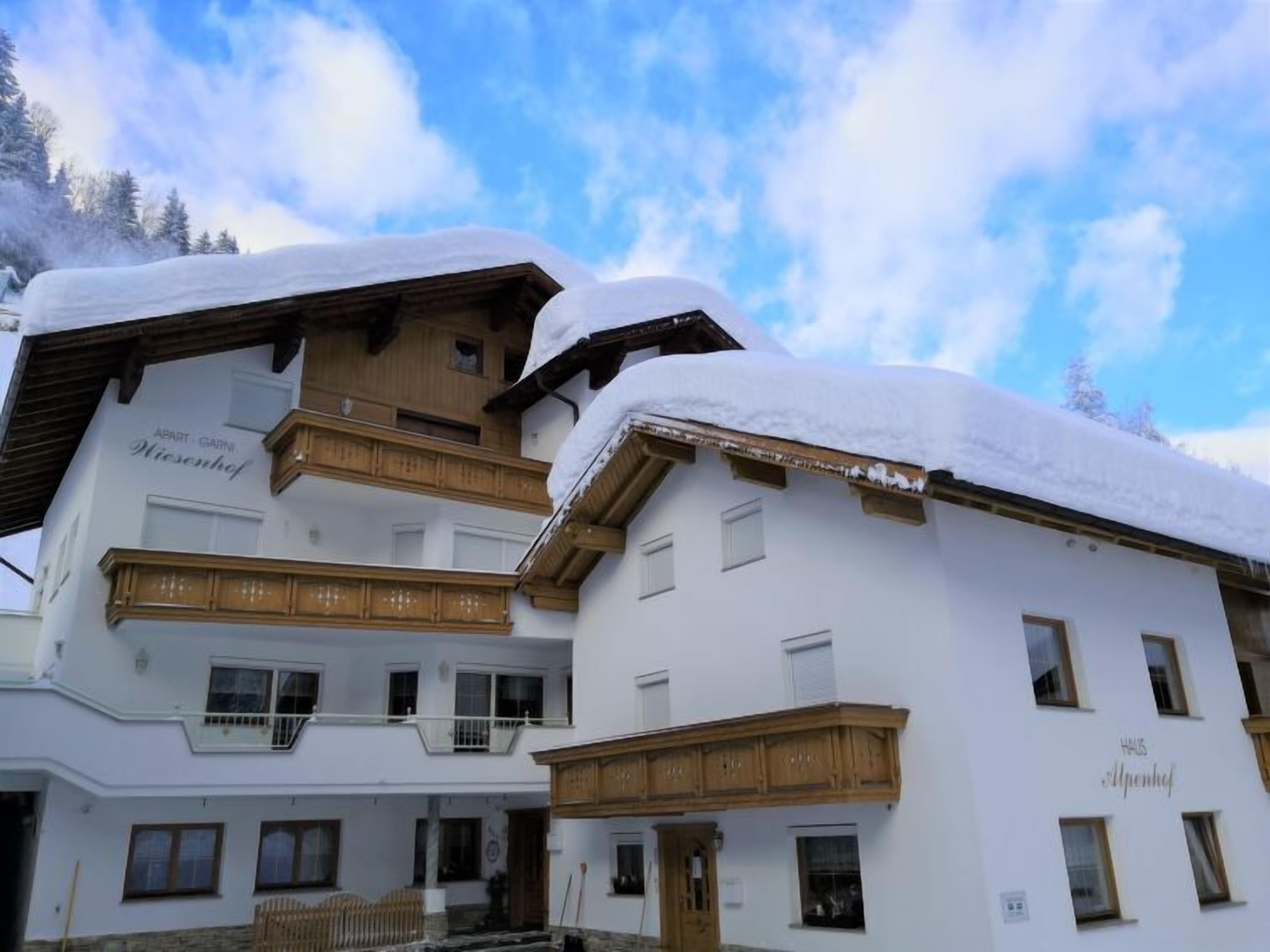 Ein zweistöckiges Gebäude mit einem Holzbalkon und einem Schild mit der Aufschrift 'Hof Alpenhof'.