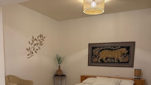 Een slaapkamer met een bed, een stoel, een nachtkastje, een lamp, een schilderij van een tijger en een trap.