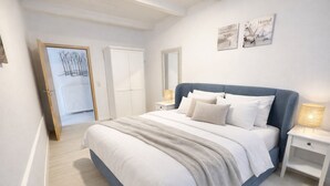 Een slaapkamer met een groot bed, witte muren, een houten vloer, een kledingkast en een spiegel.