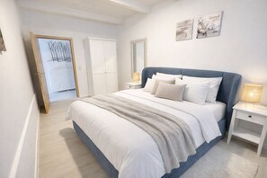 Une chambre à coucher avec un grand lit, des murs blancs, un plancher en bois, une armoire et un miroir.