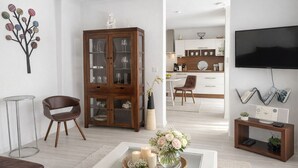 Een moderne woonkamer met een houten kast, een televisie en een salontafel met kaarsen en bloemen.