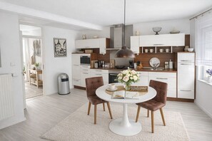 A modern kitchen with white cabinetry, a round dining table with two chairs, a hanging light fixture, and a welcome sign. - 🌿 "Huus an't Dörpsdiek" - Arrive. Take a deep breath. Feel good. (Krummhörn)
