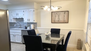 Una cocina moderna con armarios blancos, encimera de granito y un comedor con mesa de vidrio y sillas oscuras.
