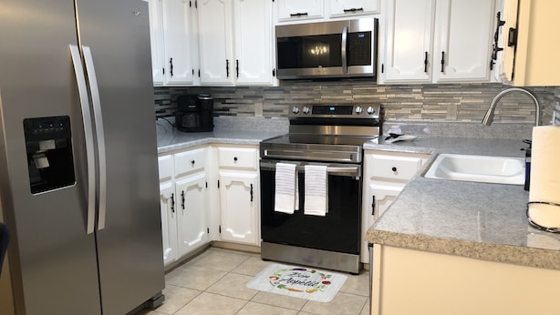 Una cocina moderna con gabinetes blancos, electrodomésticos de acero inoxidable, un microondas integrado y un lavabo.