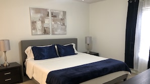 Un dormitorio ordenado con una cama, dos mesitas de noche y un buró.