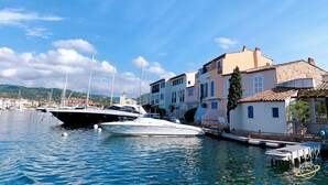 A marina with boats docked, a white building with blue shutters, and a clear blue sky. - 2 BEDROOM HOUSE IN PORT COGOLIN (with pontoon for boat) (PORT COGOLIN)