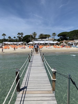 A wooden pier leading to a beach with orange lounge chairs and umbrellas.