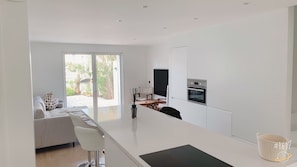A modern kitchen with a large island, a dining area with a sofa and chairs, and a view of a garden through the sliding doors.