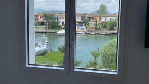 A view through a window of a canal with boats, colorful buildings, and greenery. - 2 BEDROOM HOUSE IN PORT COGOLIN (with pontoon for boat) (PORT COGOLIN)