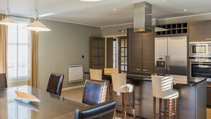Una cocina moderna con electrodomésticos de acero inoxidable, una isla central con taburetes y un comedor con mesa y sillas de vidrio.