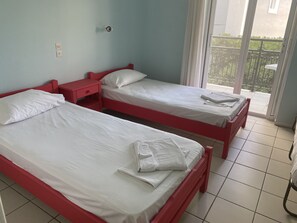A room with two beds, each with white bedding and pillows, a red nightstand, and a window with a view of greenery outside. - Hotel Asimina (Zakynthos)