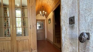 Un pasillo de madera con un gran ventanal abierto, una escalera y una araña.