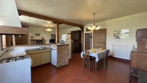 Una cocina con estufa a gas, un lavamanos y una isla de ladrillo. Hay una mesa de comedor con sillas y una araña colgante.