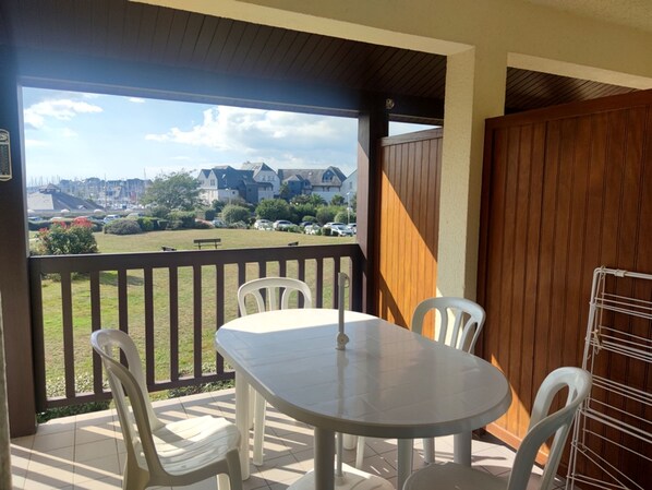 En balkon med et bord og stole, udsigt til huse og en parkeringsplads i baggrunden.