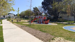 Une aire de jeux avec un toboggan et des structures d’escalade, entourée d’herbe et d’arbres.