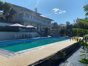 Une piscine dotée d’un bord en béton, entourée d’un bâtiment avec un balcon et un espace salon extérieur.