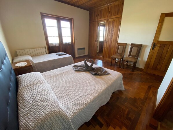 Une chambre avec deux lits, un plancher en bois, une armoire en bois et une fenêtre avec des rideaux.