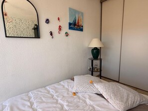 A bedroom with a bed, a mirror, wall art, a lamp, and a wardrobe.