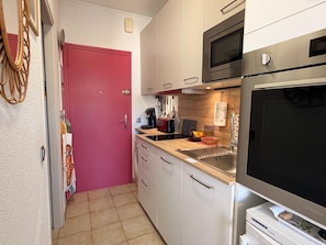 A compact kitchen with a microwave, oven, and a large TV.