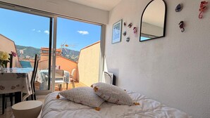 Een slaapkamer met een bed, een rond bijzettafeltje, een groot raam en een balkon met een tafel en stoelen.