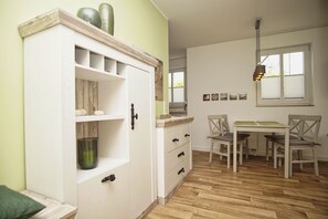 A room with a white cabinet, wooden floor, a dining table with chairs, and a hanging light fixture.