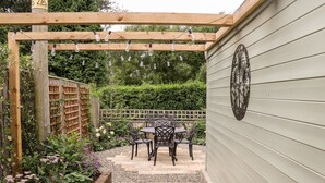 Eine Holzpergola mit Lichterketten, ein Garten mit Kiesweg und ein Tisch mit Stühlen.