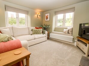 A cozy living room with a sofa, a coffee table, a radiator, and a television. - 4 Lower Folley (Chipping Campden)