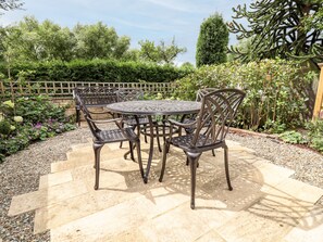 Eine Terrasse mit einem runden Tisch und vier Stühlen, umgeben von einem Kiesweg und verschiedenen Pflanzen.