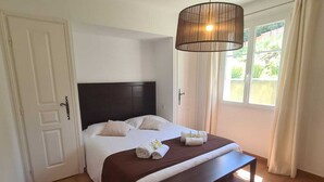 A bedroom with a bed, bedside tables, a hanging light fixture, and a view of the outdoors through a window. - Villa Avec Apercu MER ET Piscine Privee (Sainte-Maxime)