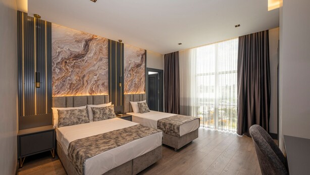 A modern hotel room with two beds, a large marble wall, and a view of the city. - World Class Airport Hotel (Arnavutköy)