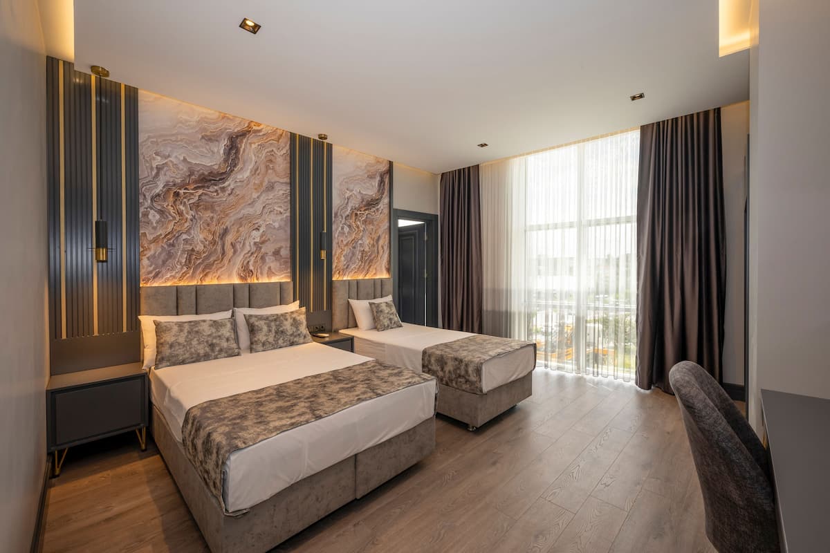 A modern hotel room with two beds, a large marble wall, and a view of the city.