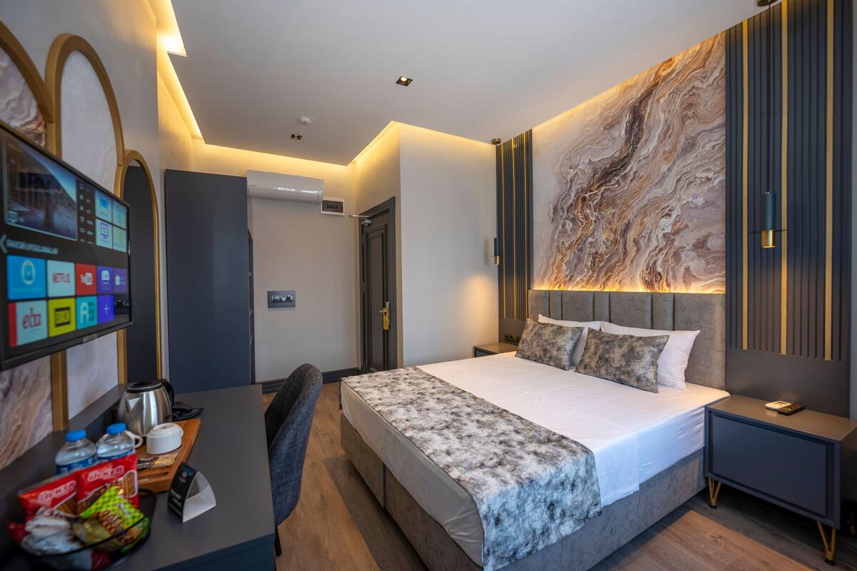 A modern hotel room with a large bed, a desk with a coffee maker, a TV, and a marble-patterned wall.