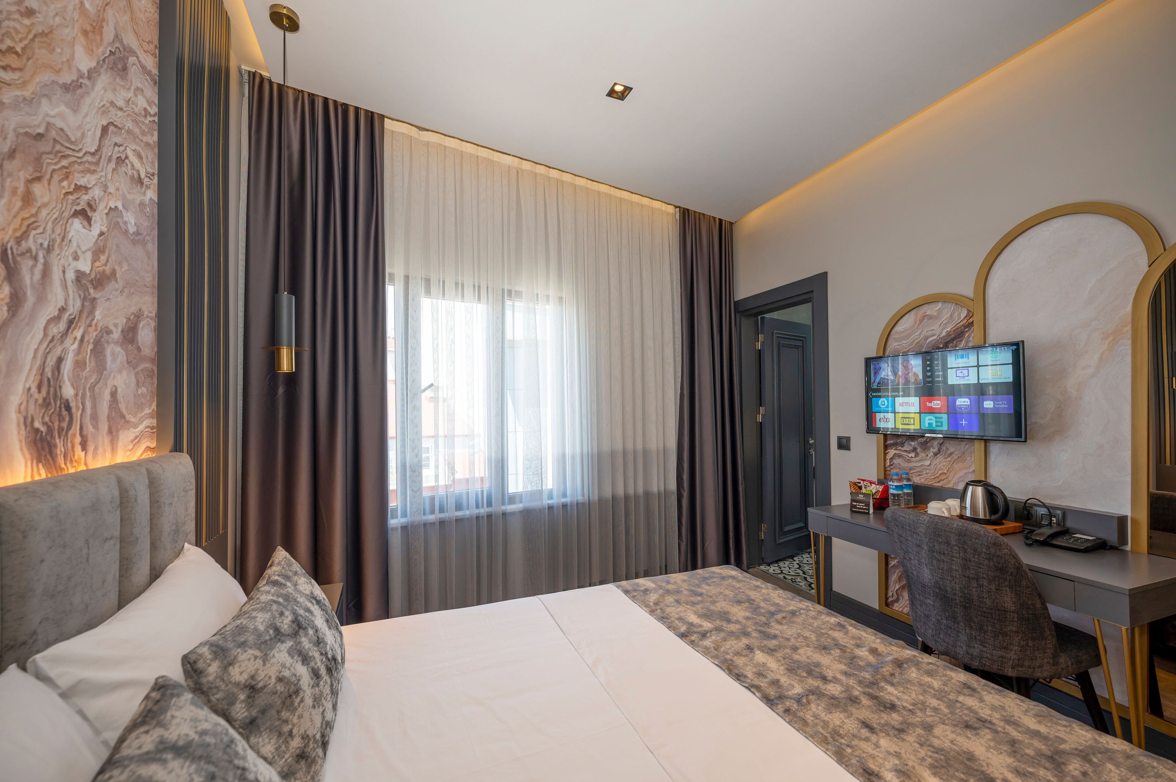 A modern hotel room with a large bed, a desk with a computer, and a television.