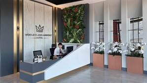 A reception desk at the World Class Airport Hotel with a modern design, including a marble wall, a digital screen, and a reception area with a plant wall and white flowers. - World Class Airport Hotel (Arnavutköy)