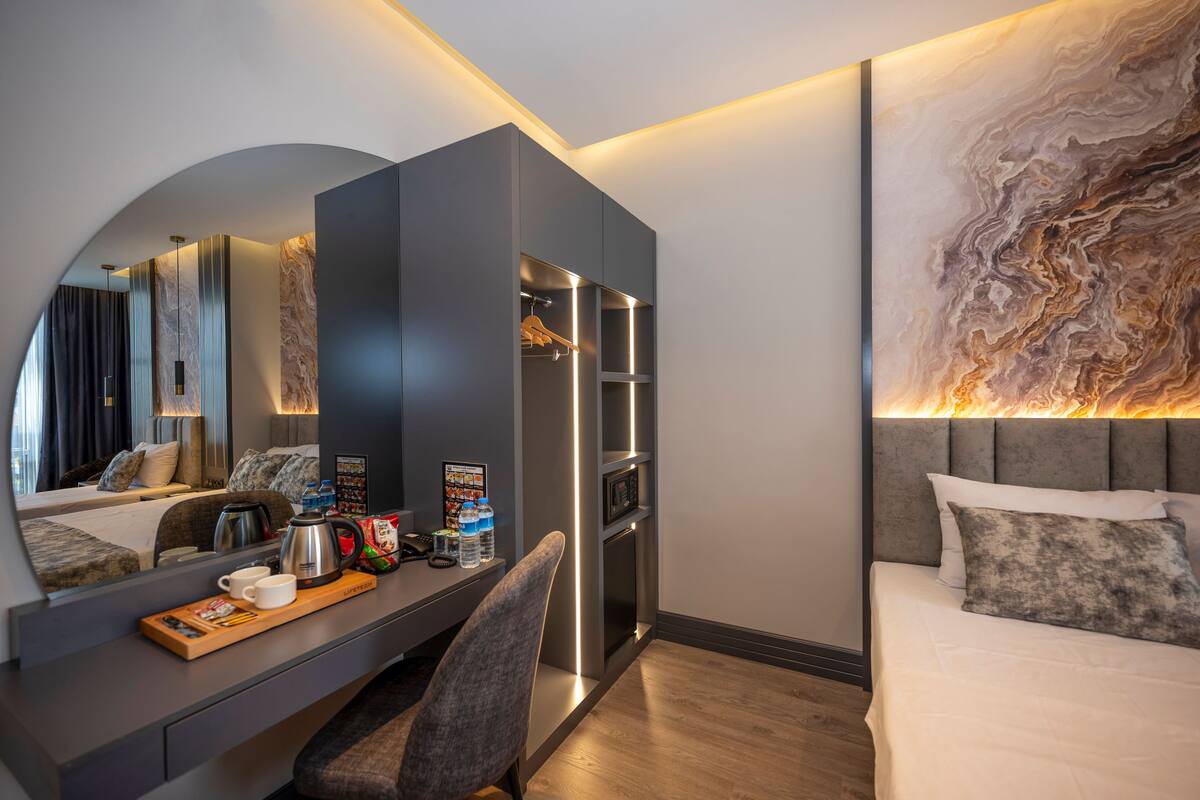 A modern hotel room with a large bed, a desk with a coffee maker, a microwave, and a large mirror.
