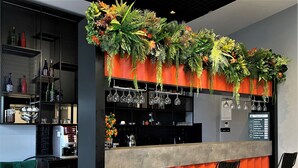 A bar area with a counter, three black bar stools, a green chair, shelves with bottles, and a menu board. - World Class Airport Hotel (Arnavutköy)