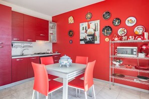 Une cuisine rouge avec des meubles blancs, une table à manger avec des chaises rouges et divers appareils de cuisine.