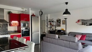 Une cuisine moderne avec des meubles de rangement rouges, une table à manger noire et un canapé gris.