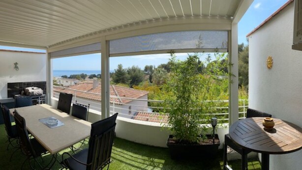 Un balcon abrité, doté d’une table et de chaises, d’une plante en pot et offrant une vue sur la mer et les bâtiments.