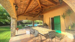 En uteplats med en träpergola, ett bord och stolar, och utsikt över en swimmingpool.
