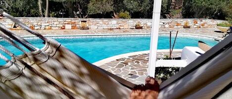 Relax by the serene pool surrounded by lush greenery and a hammock.
