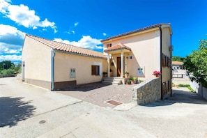 A two-story building with a tiled roof, a stone entrance, and a paved driveway.